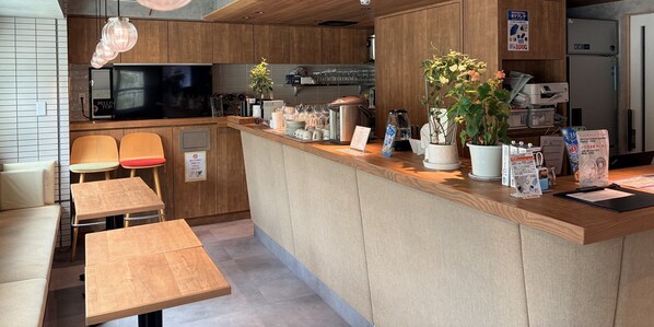 A modern kitchen with wooden cabinets, a built-in oven, and a coffee machine. There are two chairs and a table, and a potted plant on the counter. - Tokyo Tower View Guest House (Tokyo)