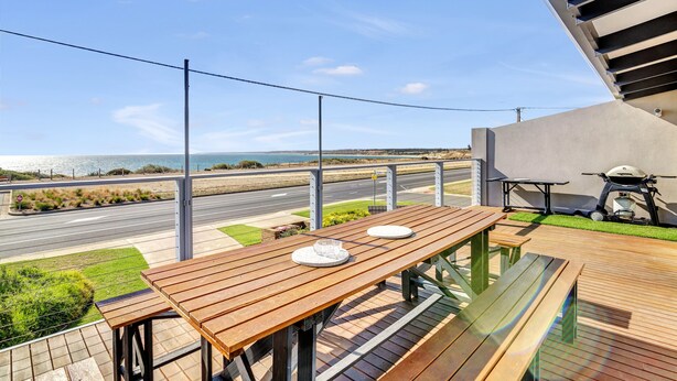 A wooden deck with a table and chairs overlooking a road and beach. - Queensland South (Aldinga Beach)