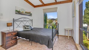 A bedroom with a bed, a nightstand, a window with a view, and a painting on the wall. - Queensland South (Aldinga Beach)
