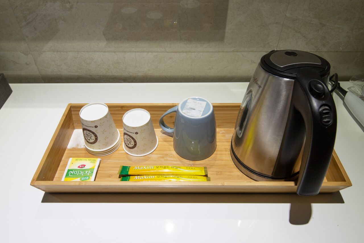 A tray with a coffee maker, two mugs, and two packets of Maxim tea on a wooden tray.
