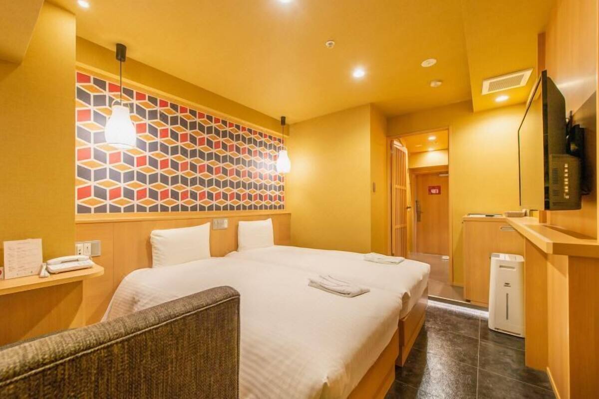 A hotel room with a large bed, a small desk, a television, and a wall with a geometric pattern.