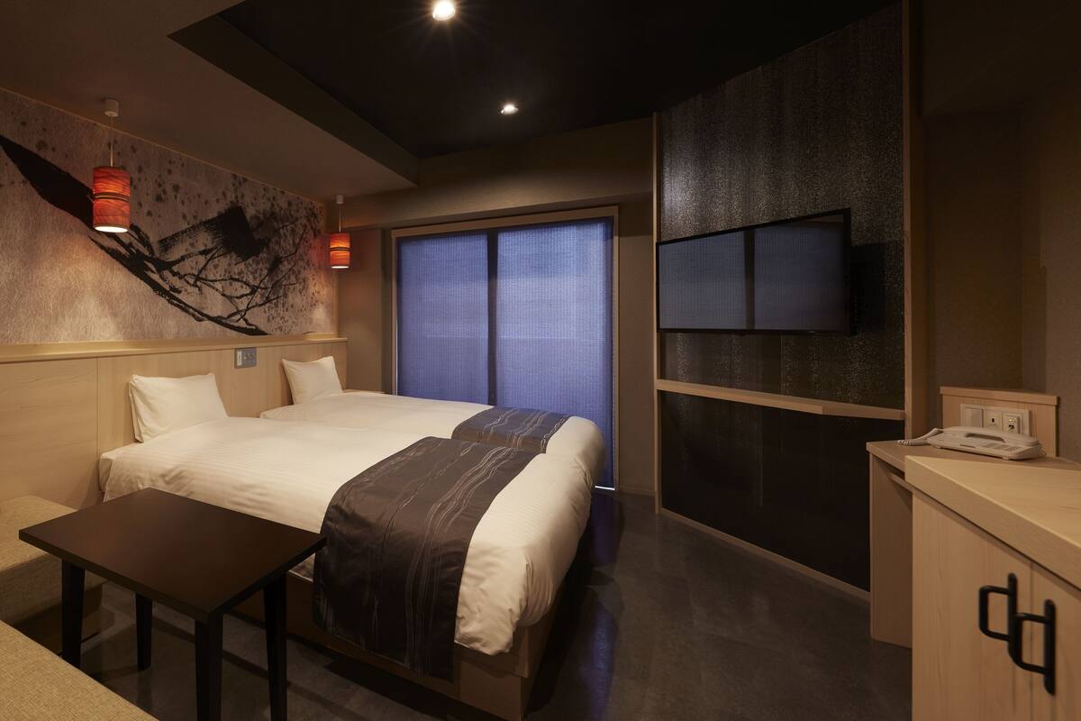 A hotel room with a bed, a desk, a chair, a TV, and a window with blinds.