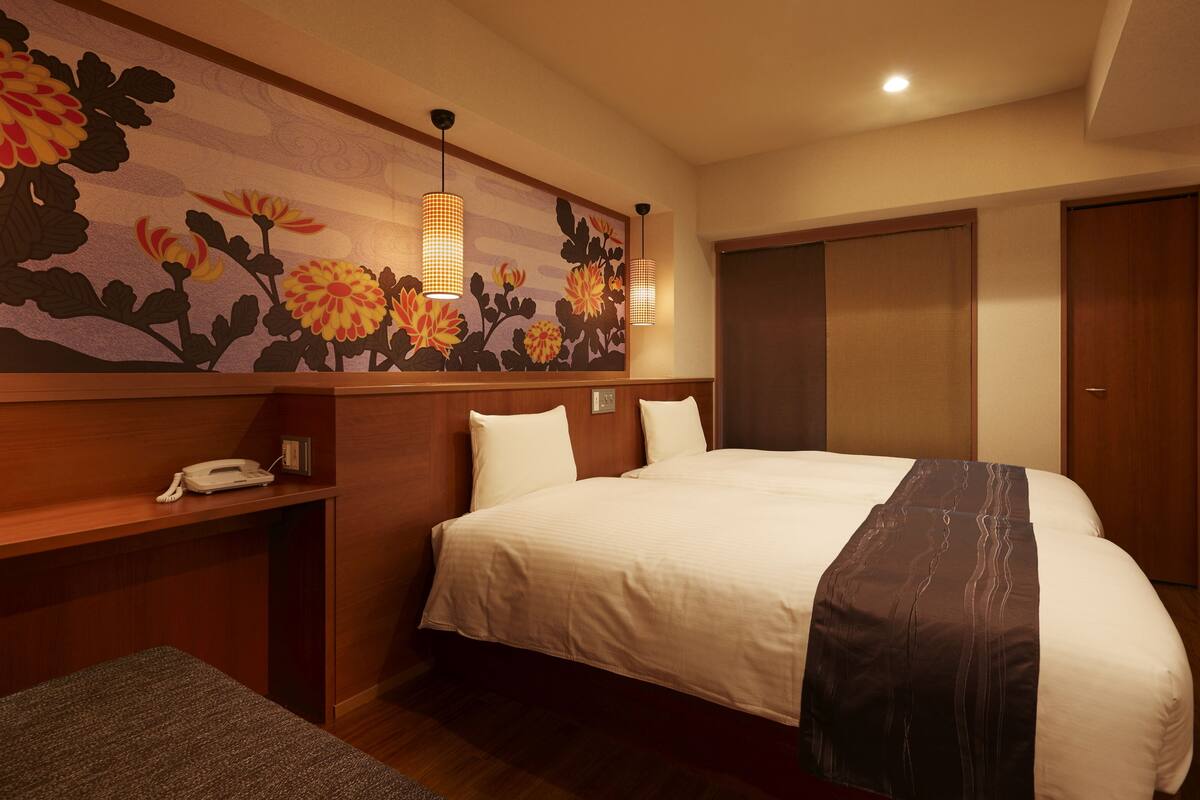 A hotel room with a large bed, a desk with a telephone, a wall-mounted TV, and a floral mural.