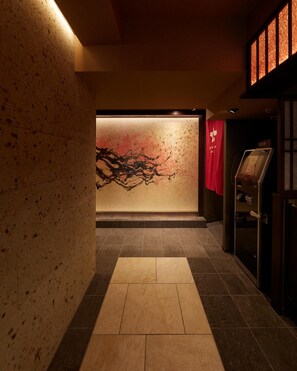 A hallway with a textured wall, a red cloth hanging, and a display case. - Sakura Sky Hotel (Tokyo)