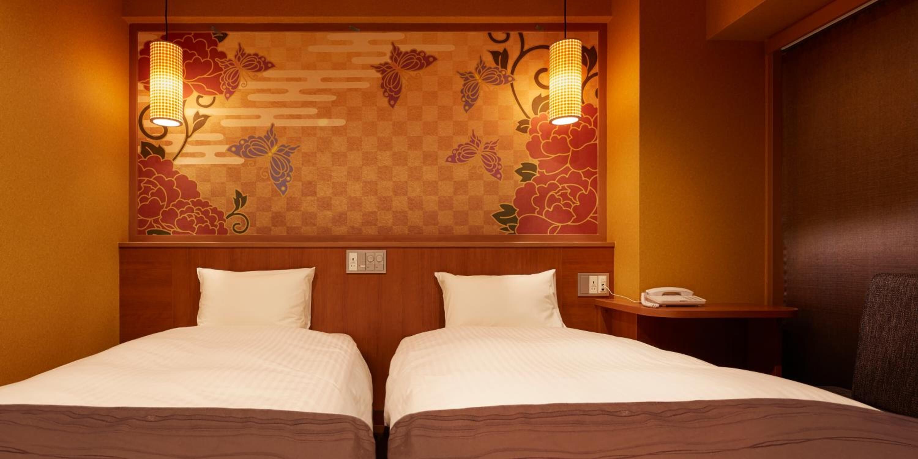 Habitación de hotel con dos camas, cabecero de madera, pared decorativa con motivos florales y dos lámparas de pared.