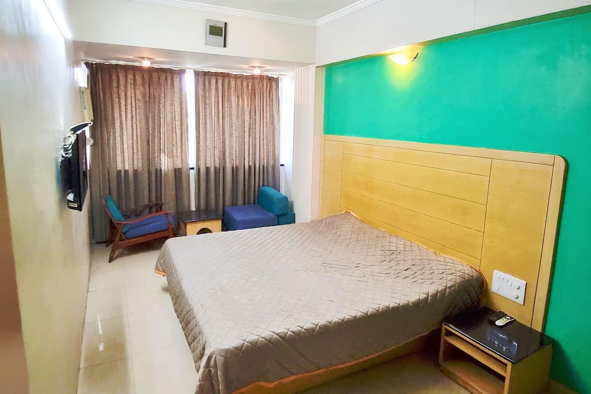 Habitación de hotel con cama, escritorio, silla y una pared de acento verde.