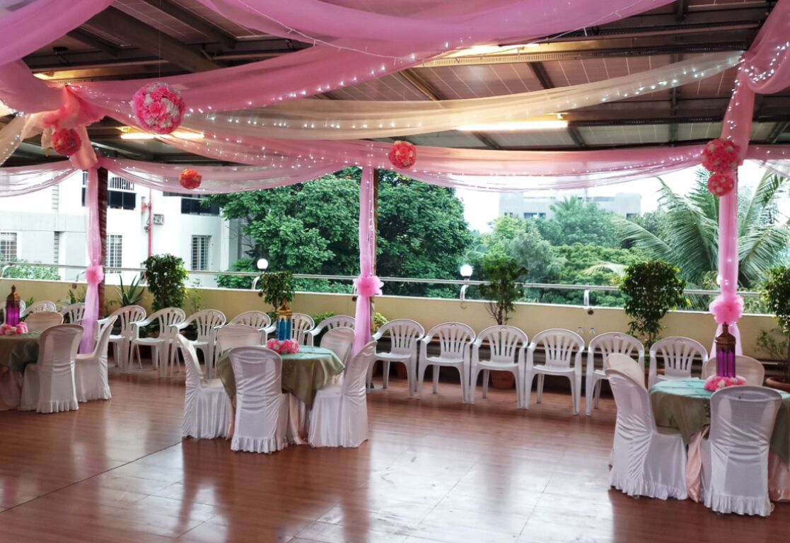 An indoor event space with tables and chairs, draped with pink fabric and floral decorations.