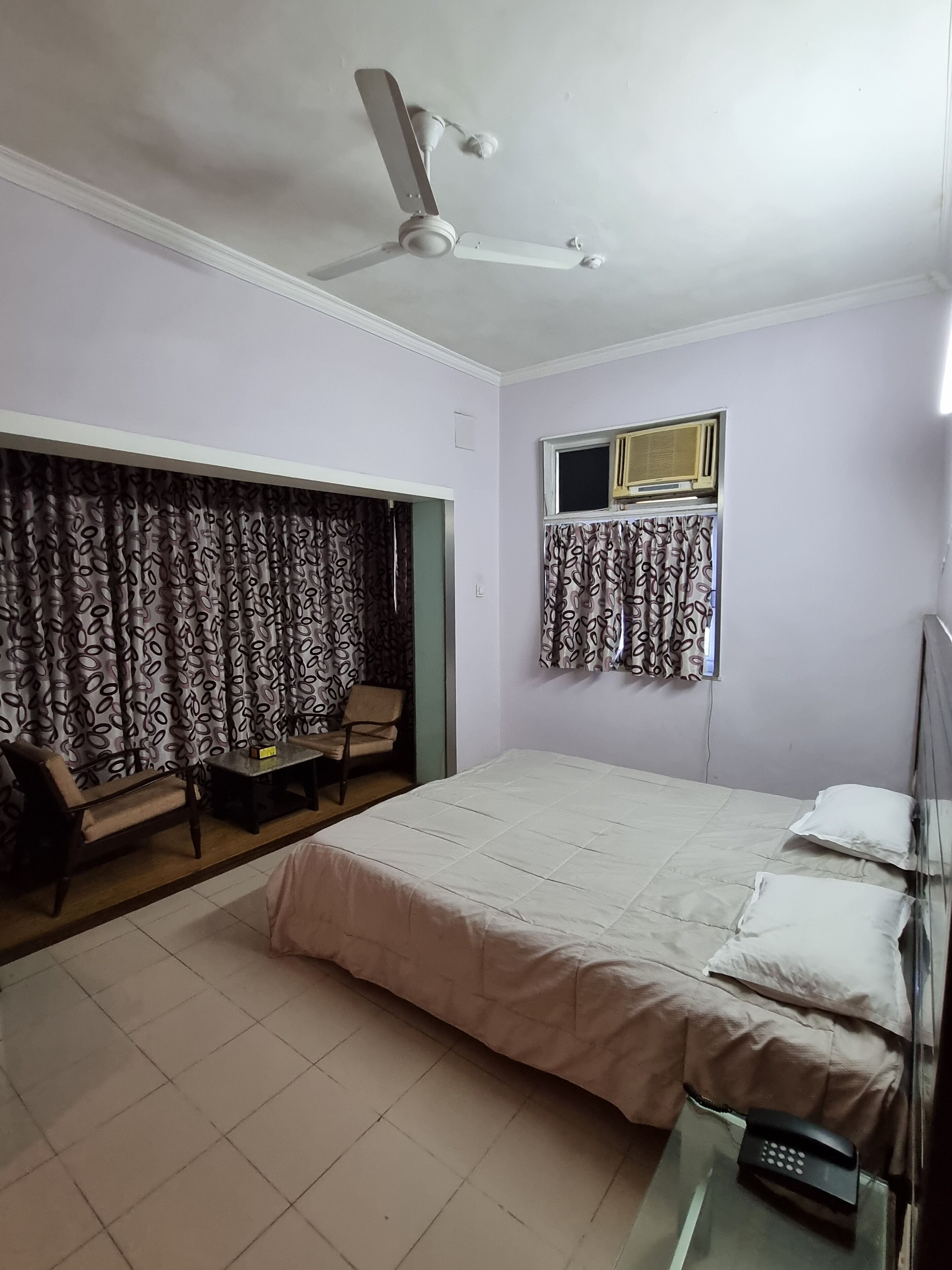 A bedroom with a bed, a chair, a table, a ceiling fan, and a window with curtains.