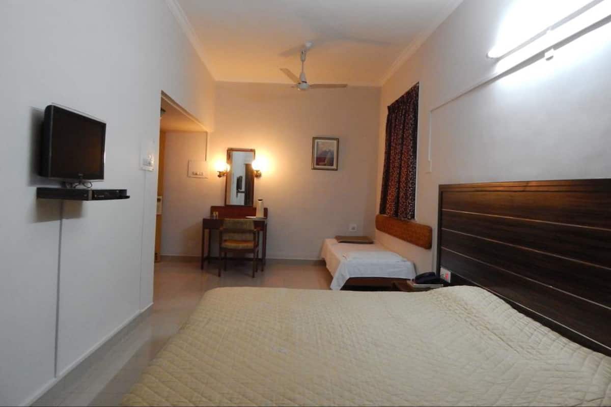 Habitación de hotel con cama, escritorio con silla, televisor, ventilador de techo y ventana con cortinas.