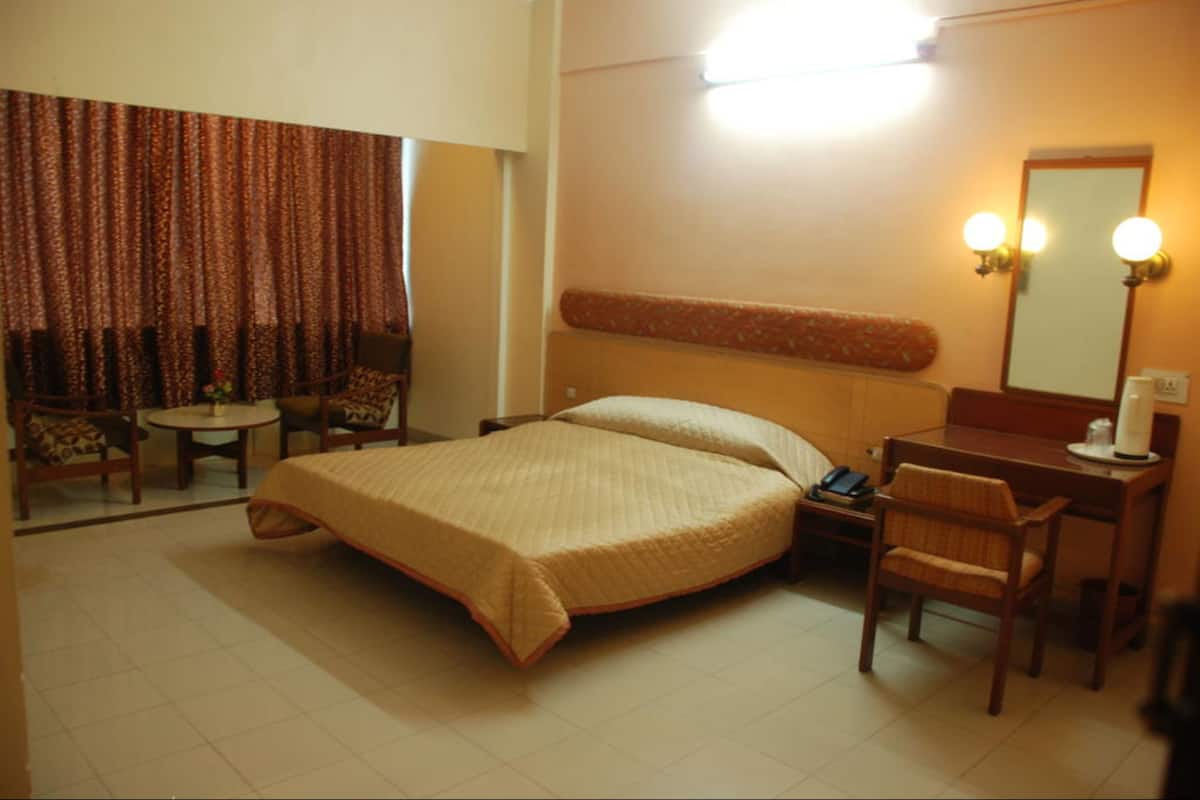 Una habitación de hotel con cama, escritorio, silla, mesita y espejo.