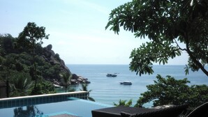Zona junto a la piscina con sillones de descanso, vista despejada al mar y terreno rocoso.