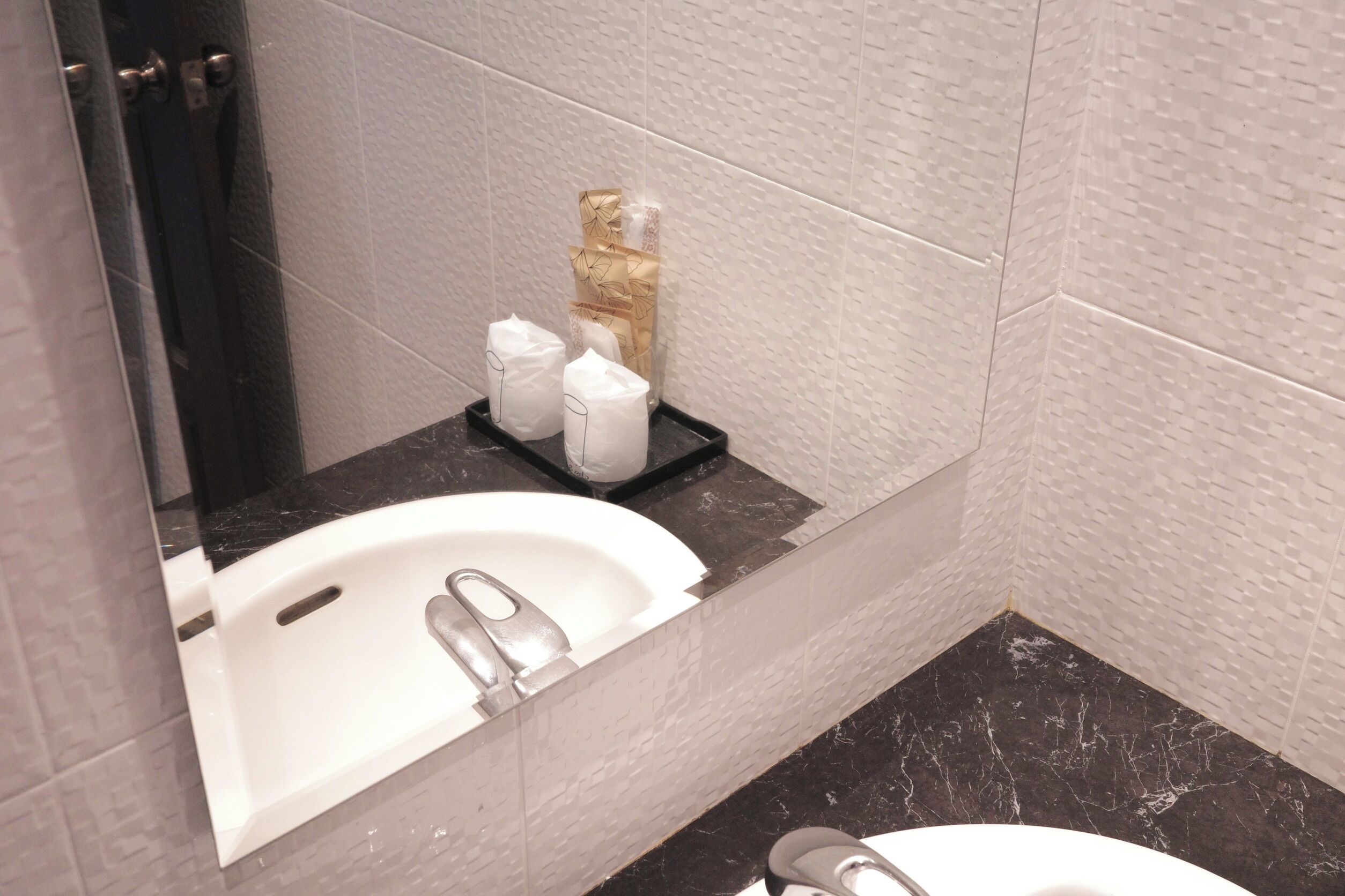 Une salle de bain avec un lavabo blanc, un plan de toilette en marbre foncé et un miroir qui reflète le lavabo. On y trouve des serviettes et des articles de toilette sur le plan de toilette.