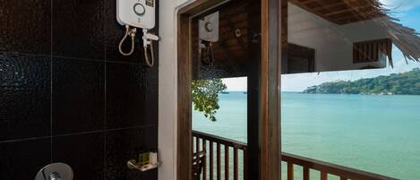A bathroom with a shower, a toilet, and a sink. There is a wooden deck with a railing overlooking a body of water.