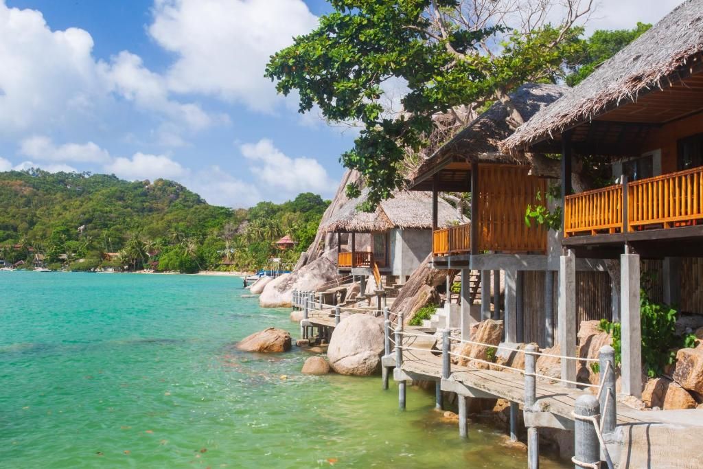 Overwater bungalows with thatched roofs, wooden railings, and clear turquoise water.