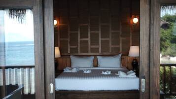 A wooden-framed bedroom with a bed, two wall-mounted lamps, and a view of the ocean.