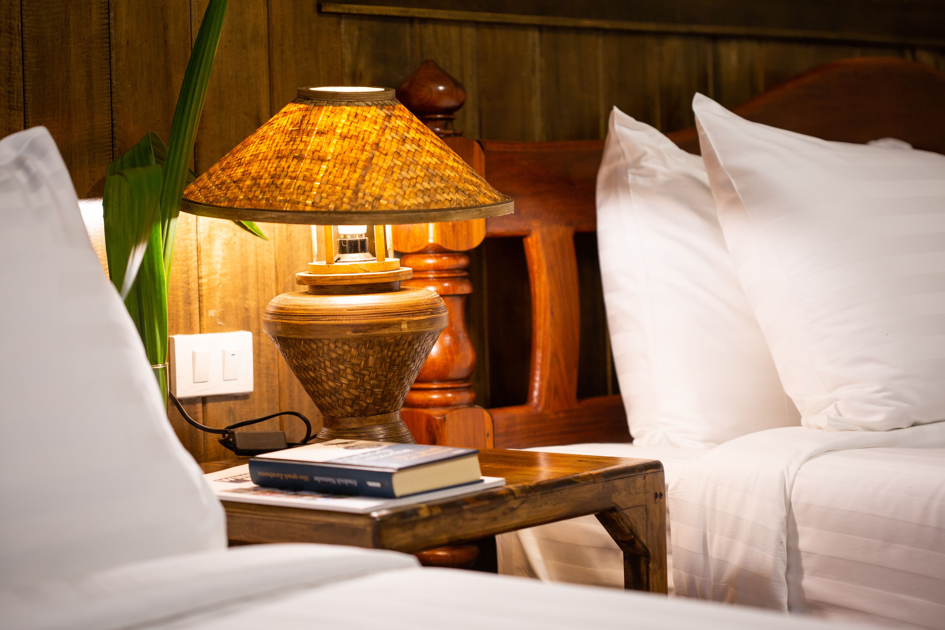 A neatly made bed with white linens, a bedside table with a lamp, and a book.