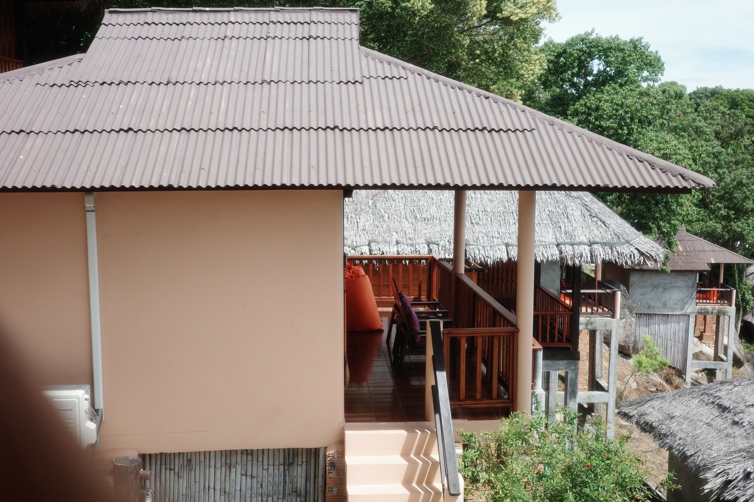 A building with a corrugated metal roof, wooden deck, and a thatched-roof structure.