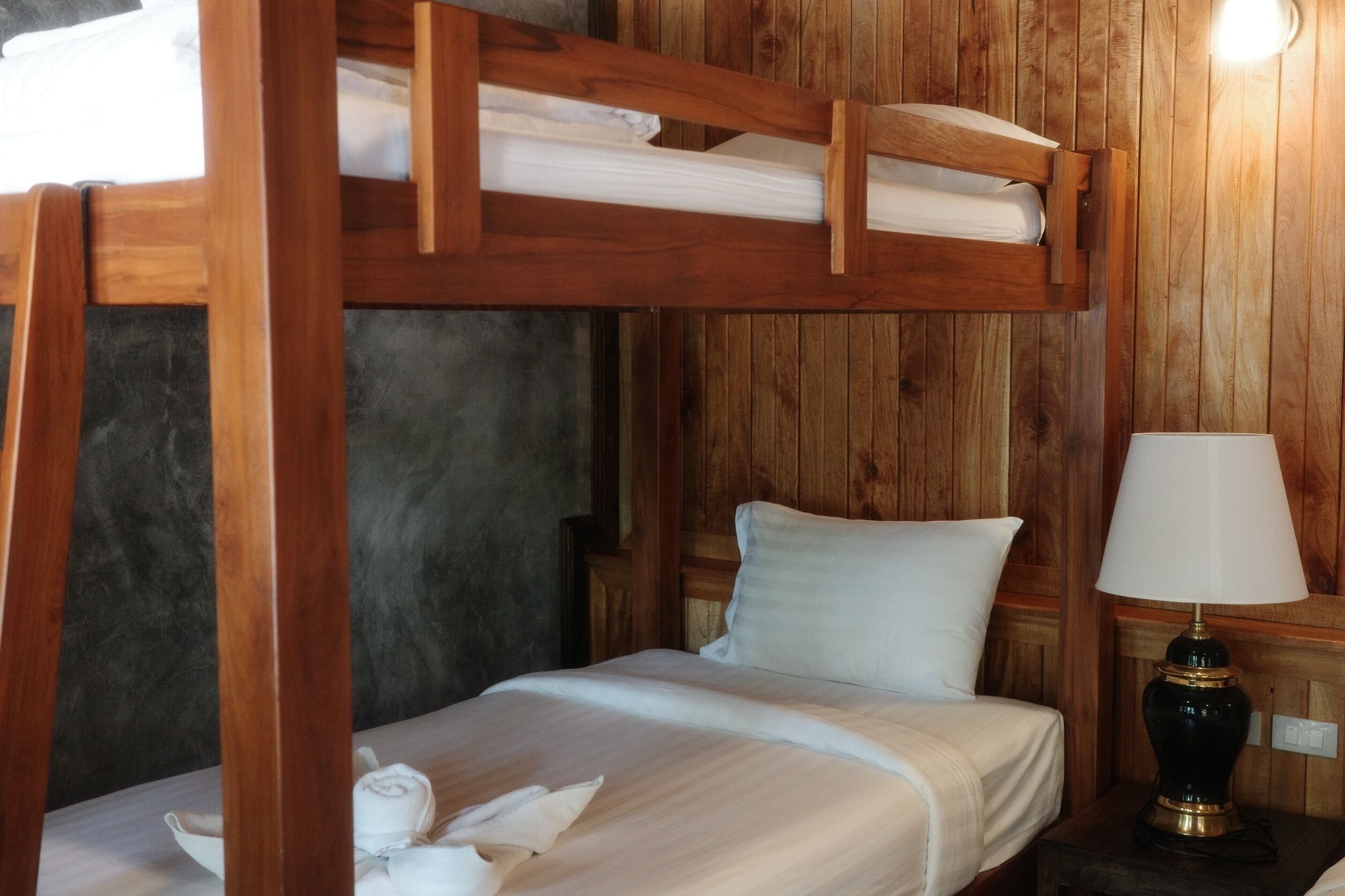 A bunk bed with white bedding, a bedside lamp, and a wooden wall.