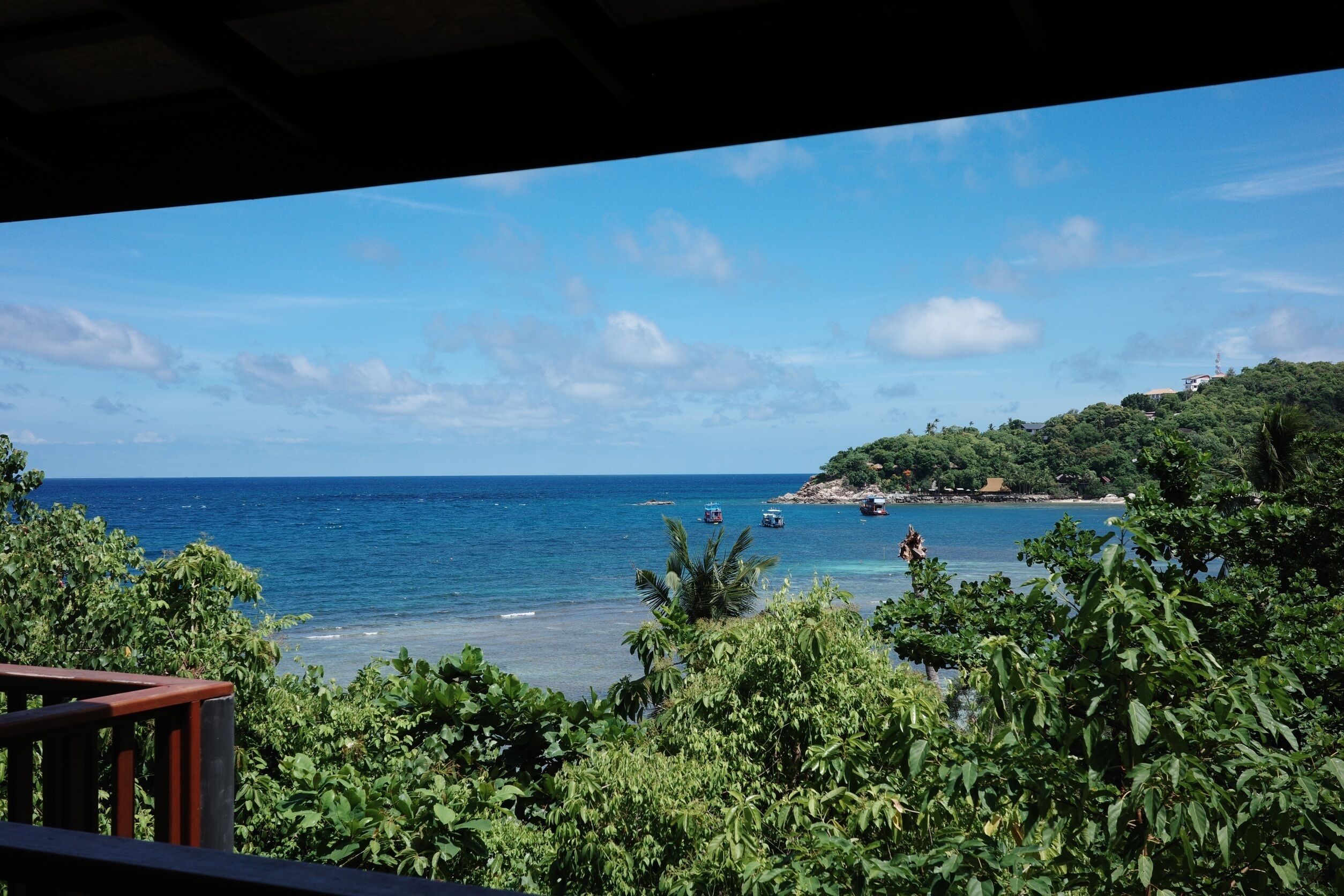 A coastal view with a clear sky, boats on the water, and lush greenery.