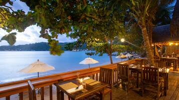 Enjoy meals in a serene setting surrounded by lush greenery and palm trees overlooking the sea.