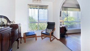 Una habitación con cómoda de madera, dos sillas, un banco, una araña y vistas amplias por las ventanas.