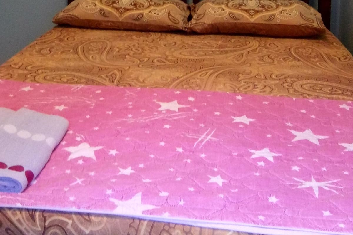 A bed with a patterned bedspread, a headboard, and a wall-mounted light fixture.