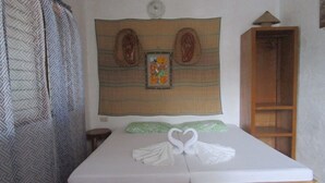 A bed with a wooden frame, a headboard with a decorative panel, a green pillow, and a towel arranged in a heart shape. - Royal Cliff Resort (San Juan)