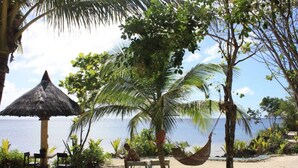 A beach setting with a thatched umbrella, a hammock, and a bench. - Royal Cliff Resort (San Juan)
