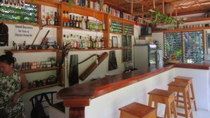 A bar area with wooden shelves stocked with books and bottles, a fan, and a sign for island souvenirs. - Royal Cliff Resort (San Juan)