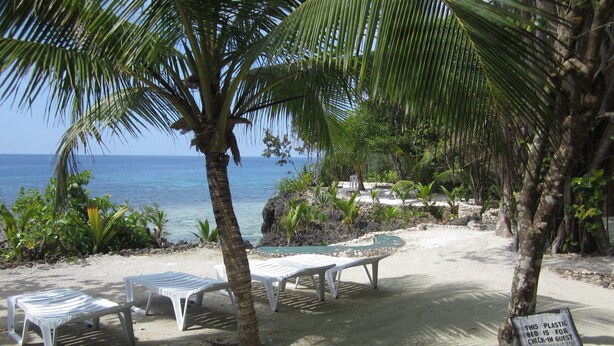 A beachside area with white lounge chairs and a sign indicating a plastic bed for check-in guests. - Royal Cliff Resort (San Juan)