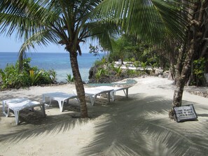 A beachside area with white lounge chairs and a sign indicating a plastic bed for check-in guests. - Royal Cliff Resort (San Juan)