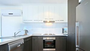 A modern kitchen with white cabinets, stainless steel appliances, and a built-in oven. - Sunset at Snapper Point (Aldinga Beach)