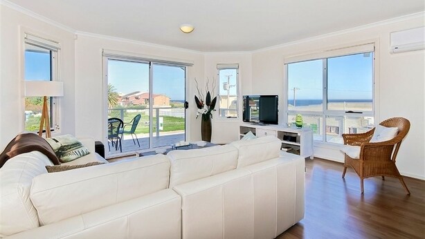 A spacious living room with a white sofa, a television, and a wicker chair. - Sunset at Snapper Point (Aldinga Beach)