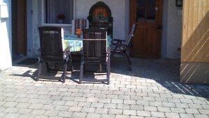 A covered outdoor seating area with a table and chairs, a wooden door, and a tiled floor. - Müllers Gästeunterkunft Gangkofen (Gangkofen)