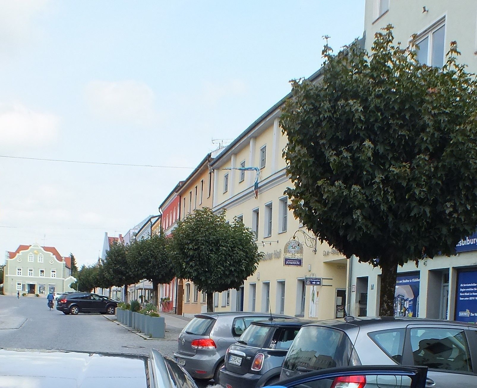 A row of parked cars along a street lined with buildings, some with visible signage.