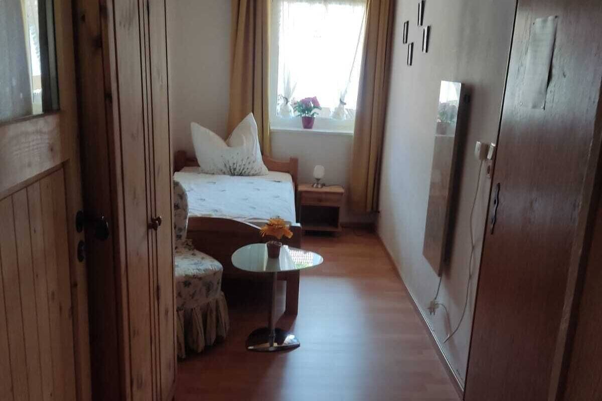 Ein Zimmer mit Bett, kleinem Tisch, einem Fenster mit Vorhängen und Holzwänden.