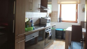 A kitchen with wooden cabinets, a microwave, a stove, and a window with blinds. - Müllers Gästeunterkunft Gangkofen (Gangkofen)