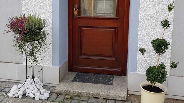 A wooden front door with a glass panel, a small potted plant to the right, and a number '22' sign above it. - Müllers Gästeunterkunft Gangkofen (Gangkofen)