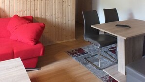 A room with a wooden ceiling, a red sofa, a dining table with chairs, and a framed picture on the wall. - Müllers Gästeunterkunft Gangkofen (Gangkofen)