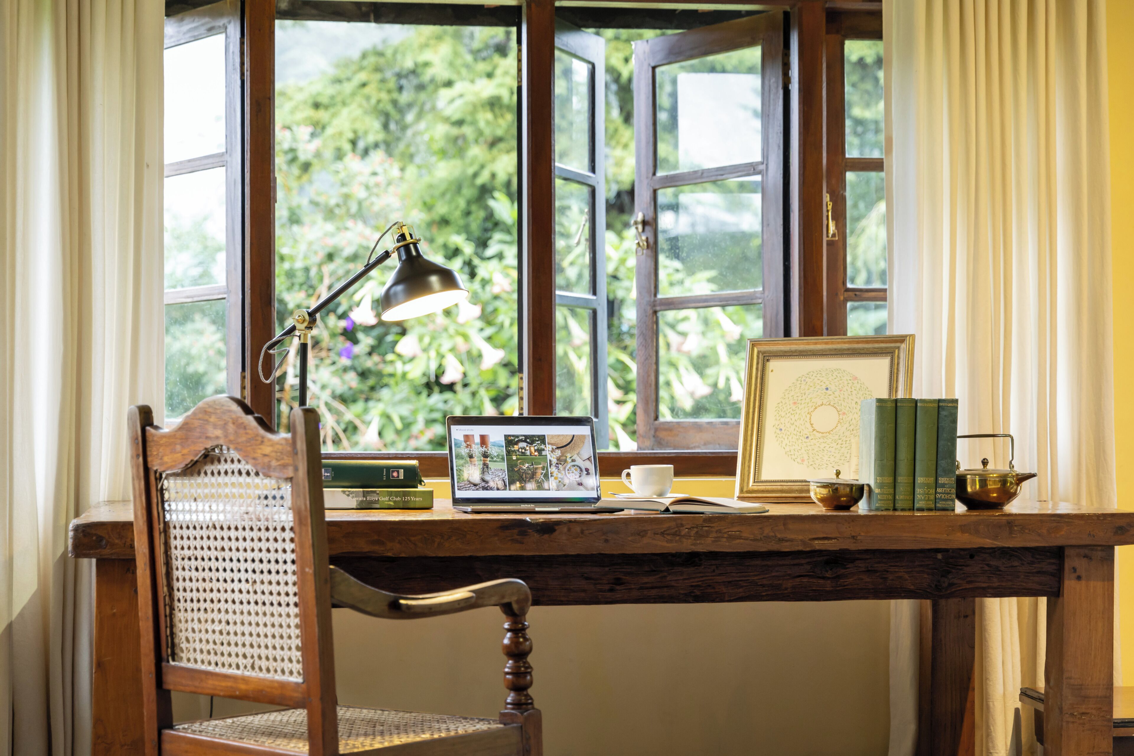 A wooden desk with a laptop, books, a teapot, and a framed picture.