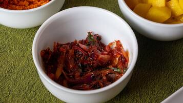 On peut voir une variété de plats servis dans des bols, dont un plat qui ressemble à un curry, un plat à base de mangue et un plat rouge et épicé, le tout disposé sur un tissu vert.
