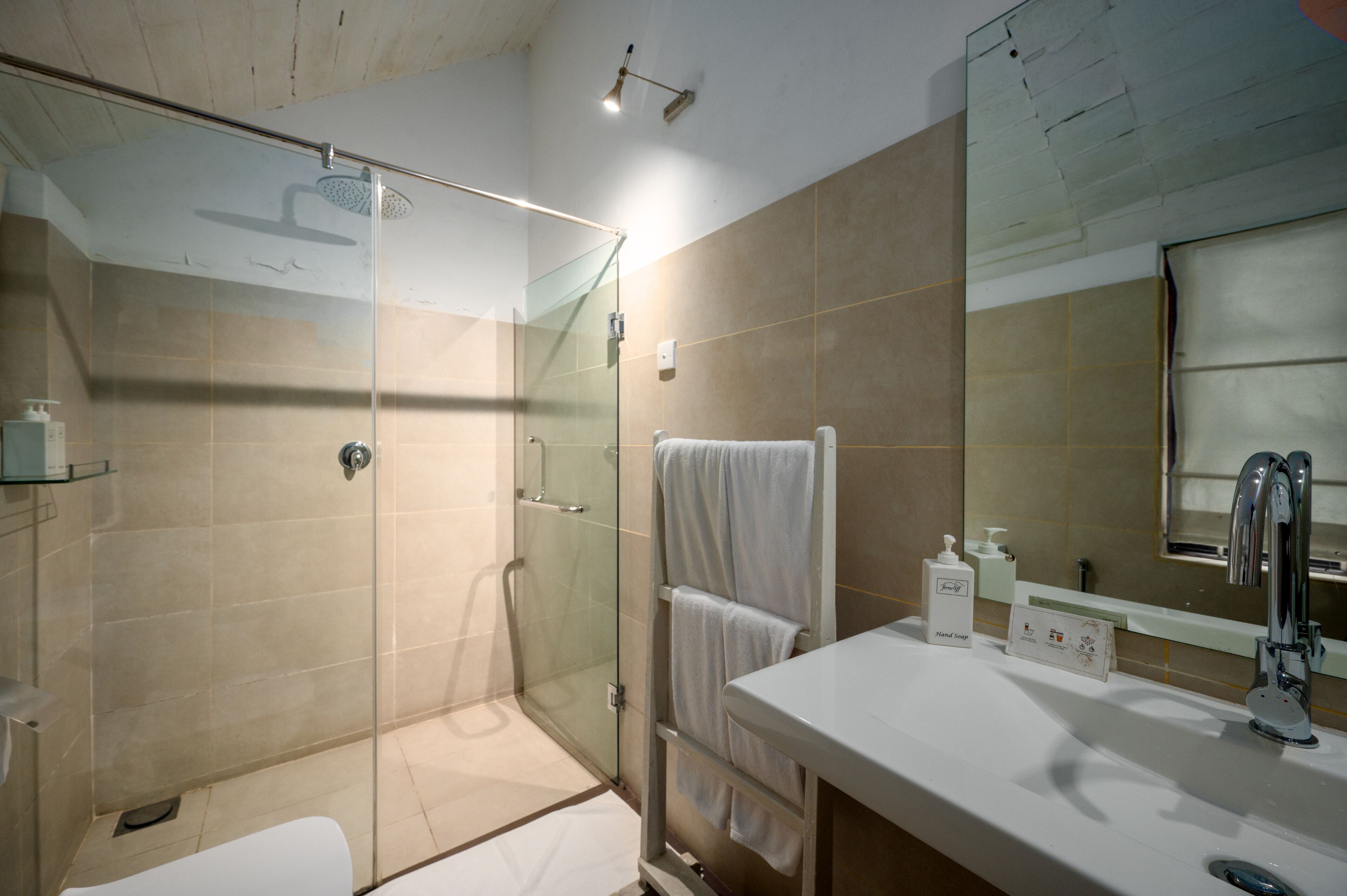 Ein modernes Badezimmer mit einer begehbaren Glasdusche, einem weißen Waschbecken und einem großen Spiegel.