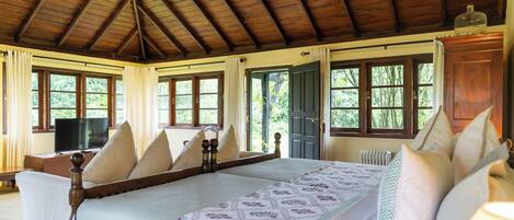 A room with a wooden ceiling, a bed with a floral bedspread, and a television on a wooden table.