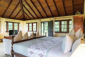 A wooden-framed bed with a floral bedspread, a television on a stand, and a view of greenery outside. - Ferncliff Bungalow (Nuwara Eliya)