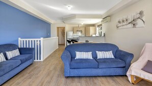 A spacious living area with a blue sofa, a white chair, and a kitchen in the background. - The Lighthouse (Port Willunga)