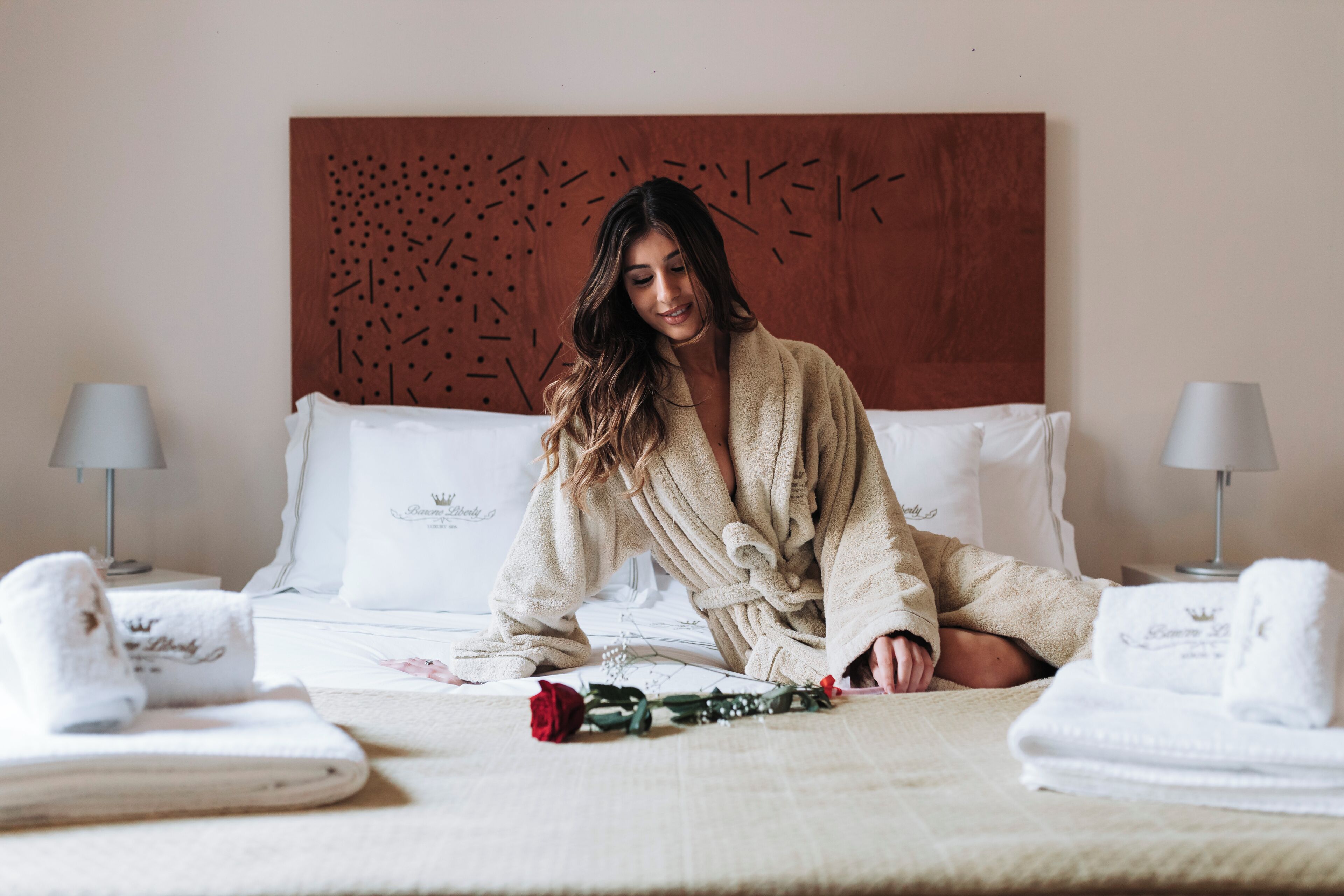 A hotel room with a bed, pillows, a headboard, and two bedside lamps.