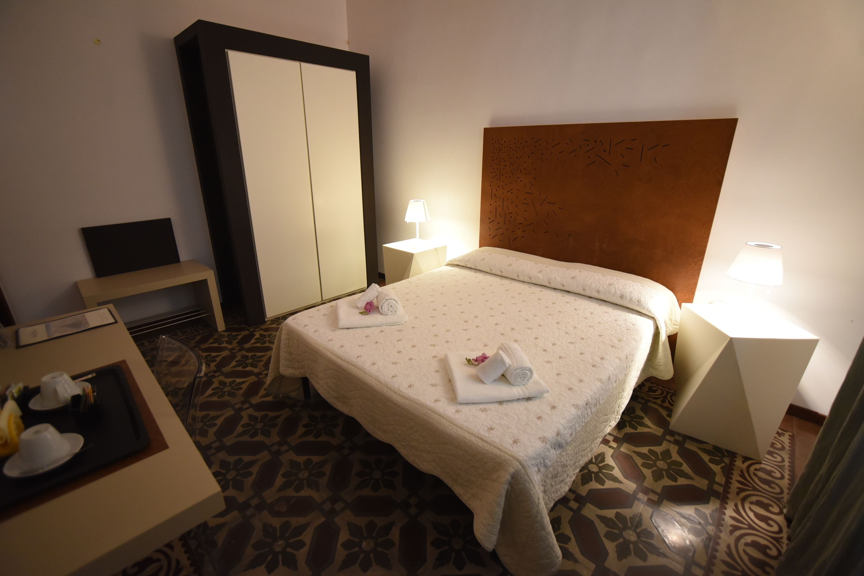 A hotel room with a bed, bedside tables, a wardrobe, and a small table with a tray of breakfast items.