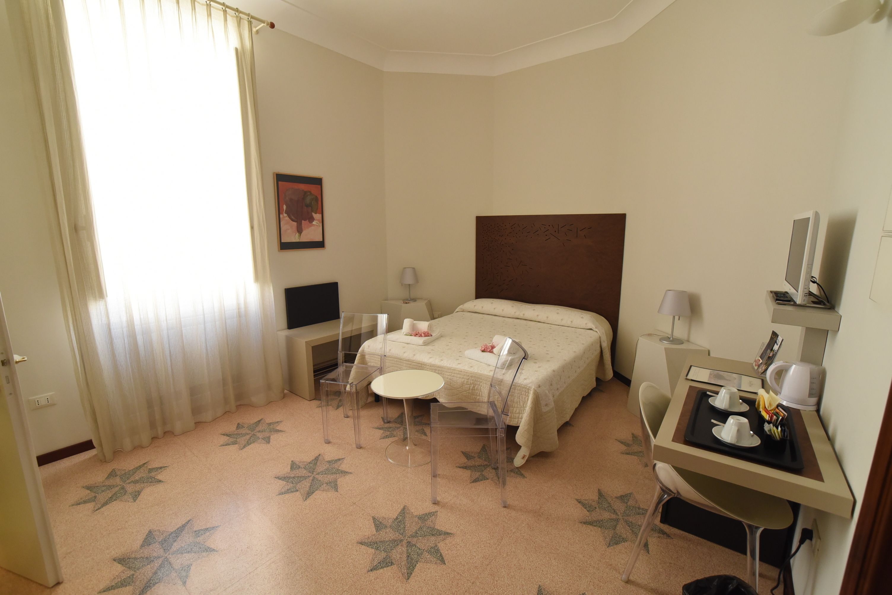 Quarto de hotel com uma cama, uma escrivaninha com computador, uma cadeira, uma pequena mesa e um chão com padrão de estrelas.