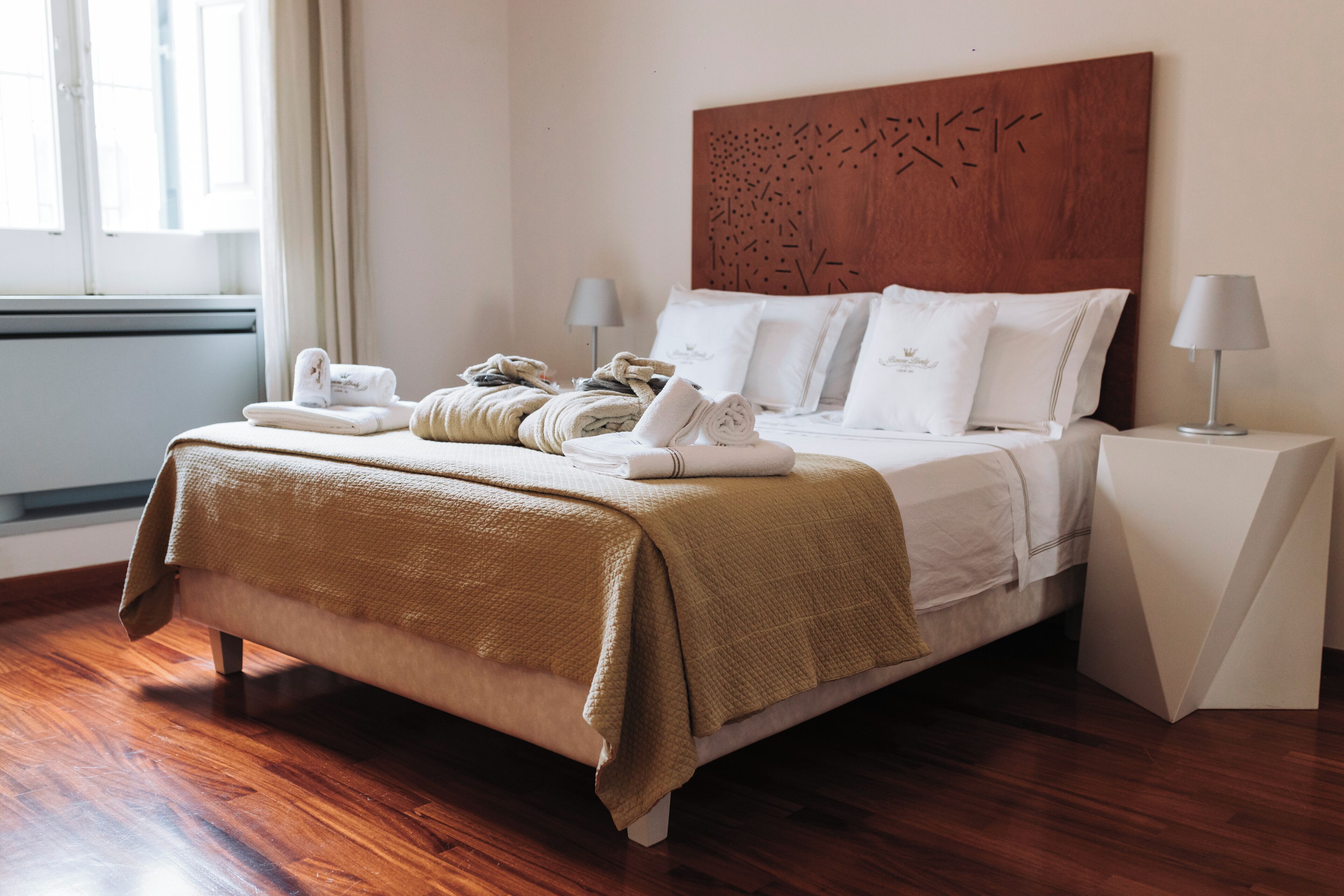 Un lit bien fait, avec une couverture marron, des oreillers blancs et des serviettes pliées, posé sur un plancher en bois.