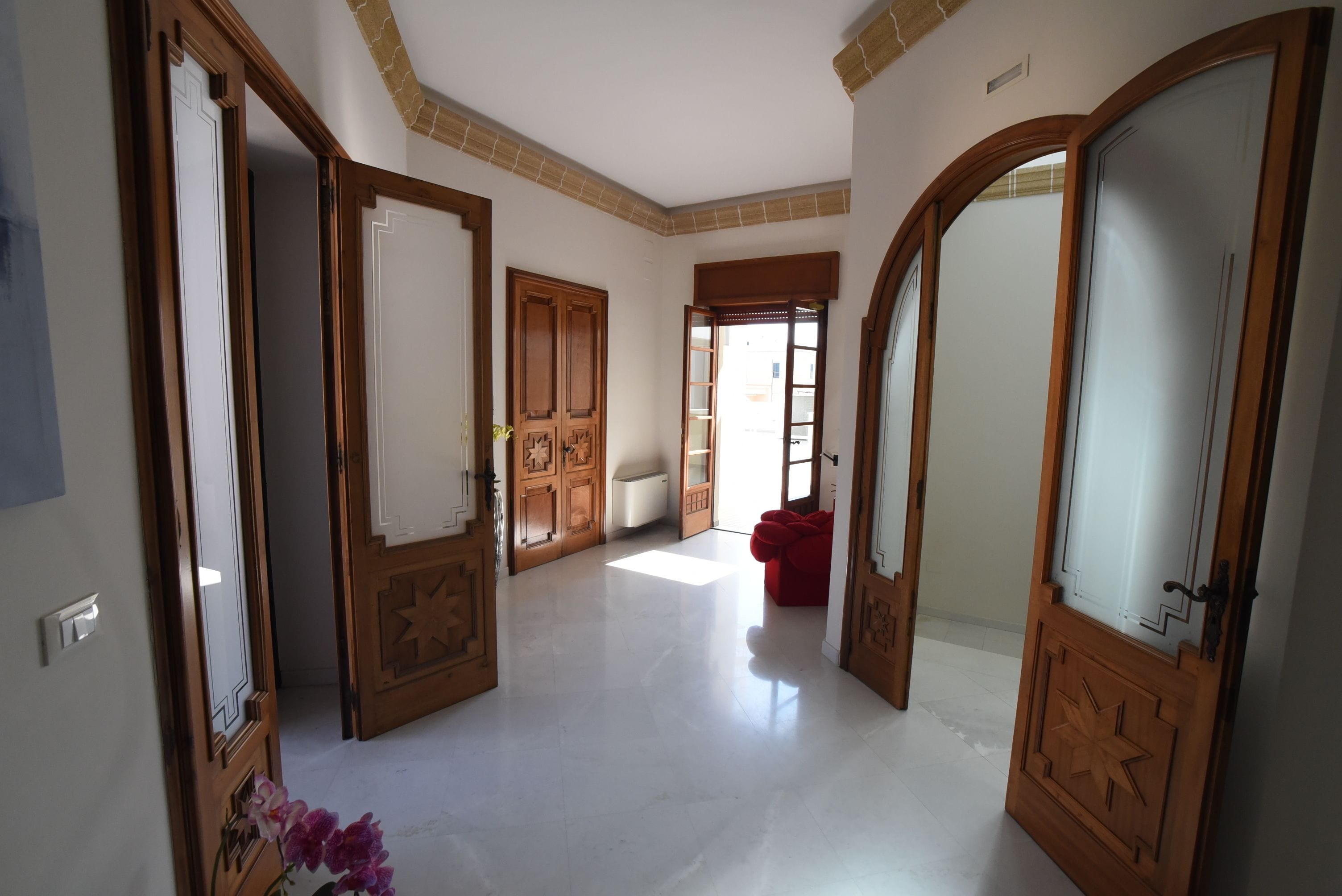 Un pasillo espacioso con puertas de madera y una silla roja, que conduce a una habitación luminosa con ventana.